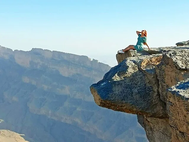 Frau sitzt am Rand einer felsigen Klippe mit Blick auf eine Schlucht