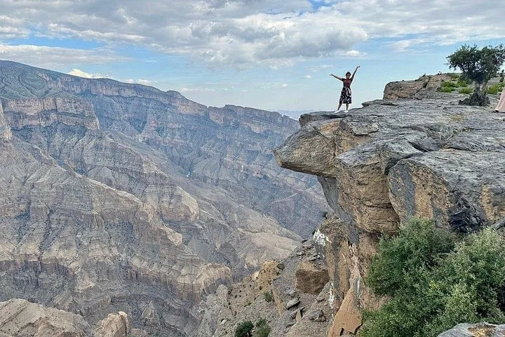Person mit erhobenen Armen am Rand einer Klippe